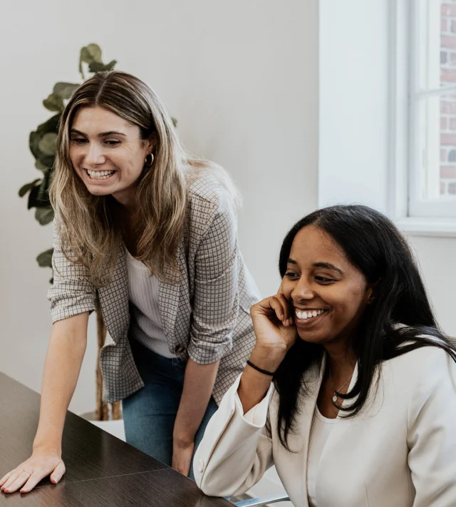 Two people smiling and looking at a computer screen in an office setting.